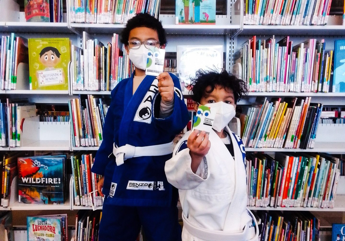 Kids with masks holding their library card to the camera